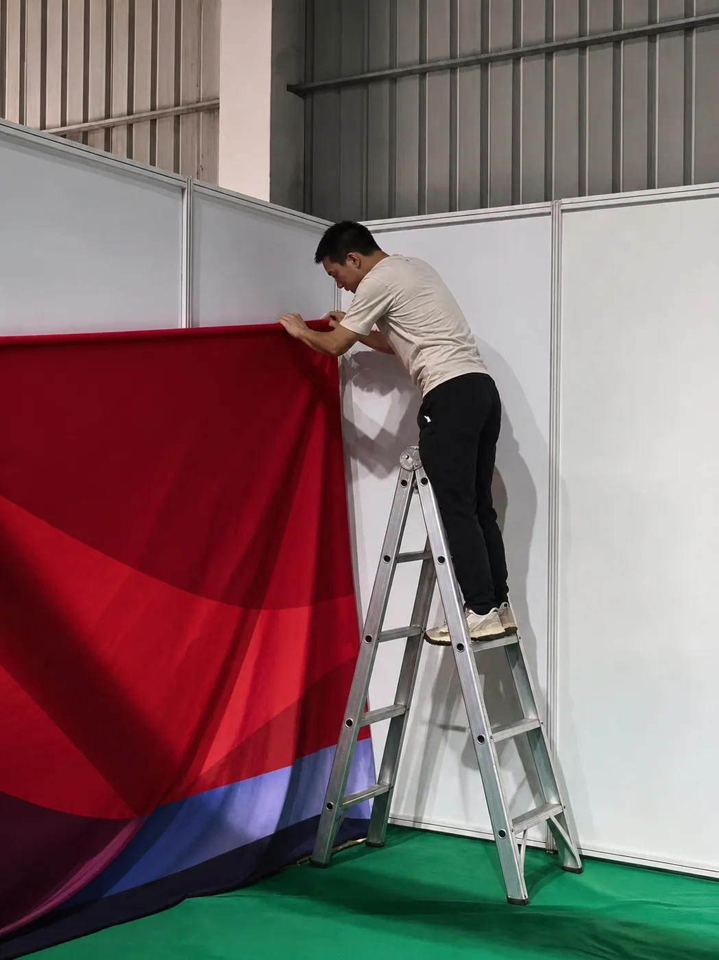 Installer using a suitable step ladder to mount a fabric graphic on a shell scheme booth