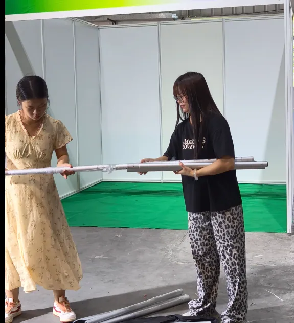 Two people assembling a sectional hanging rod for a portable fabric booth