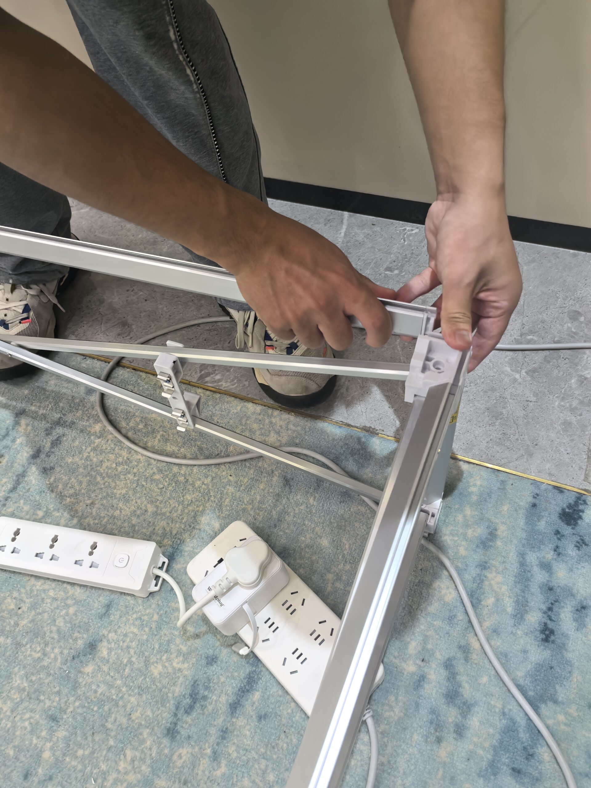 Installer positioning a metal perimeter profile at a white corner connector on a folding display frame.